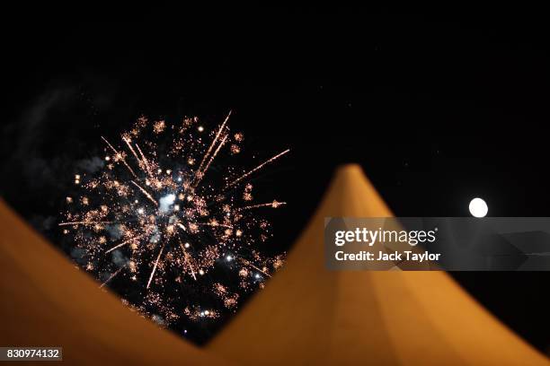 Fireworks appear above tents as the moon is illuminated in the sky during the Guca Trumpet Festival on August 10, 2017 in Guca, Serbia. Thousands of...