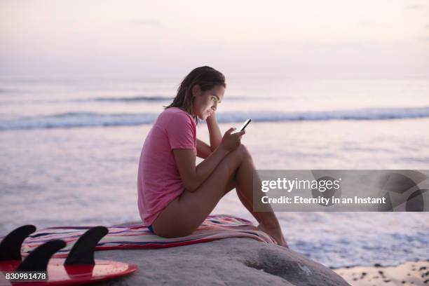 ws young woman looking at her phone while sitting by the sea - funkwelle stock-fotos und bilder
