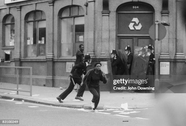 Young woman running away as policemen take cover in the doorway of a National Westminster Bank during the Brixton Riot of 11th April 1981.