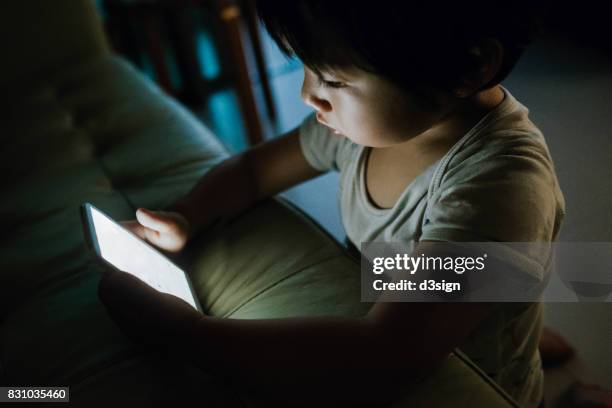 Little kid concentrated on playing with smartphone in the dark
