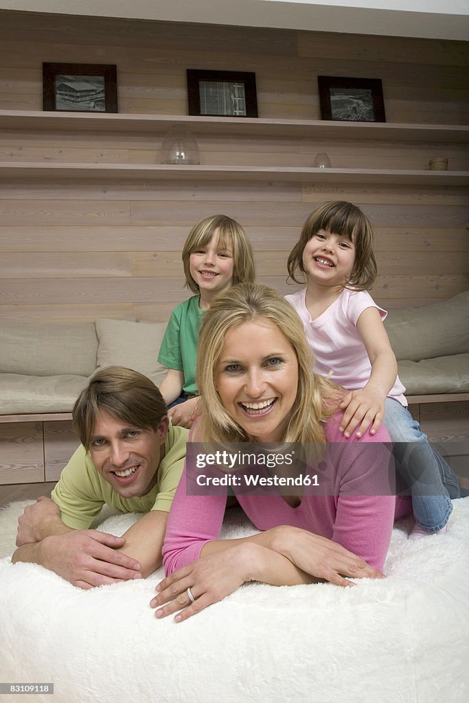 Family in living room, children sitting on parent's neck, smiling, portrait