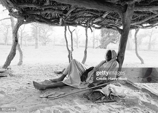 Dogon elder rests in the shade of a "Casa palava" or "to guna". Nombori, Dogon Country, Mali.