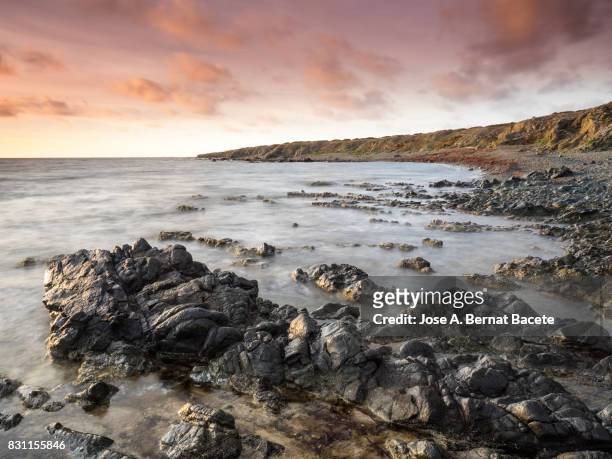 exit of the sun with a sky of clouds of orange color, on the surface of the sea, in a zone of coast and beach with rocks and waves in movement - tabarca stock pictures, royalty-free photos & images