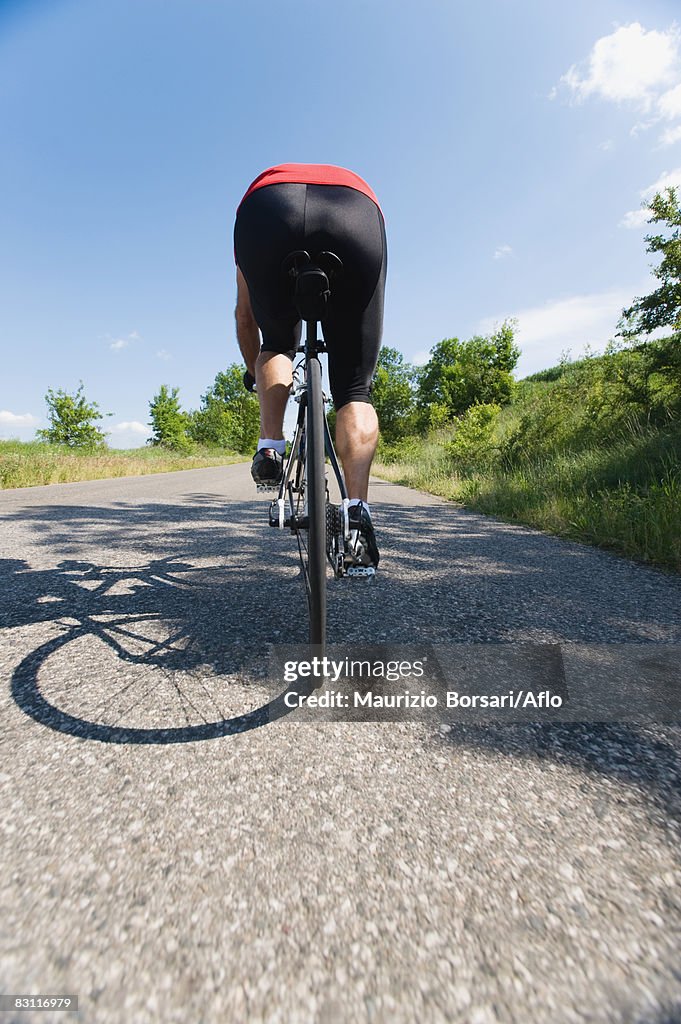 Rear view of a man cycling on road