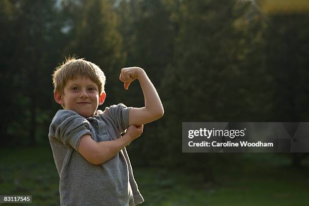 boy flexes his muscles in wilderness on camp trip. - stolz stock-fotos und bilder