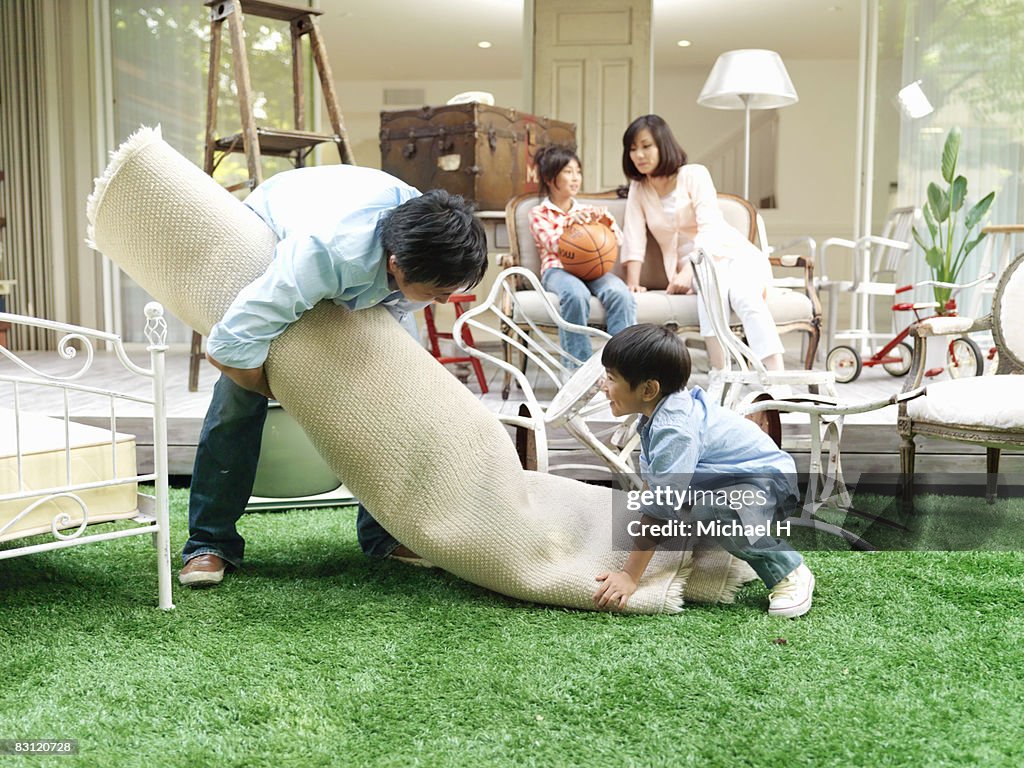 Man and boy carries carpet in yard