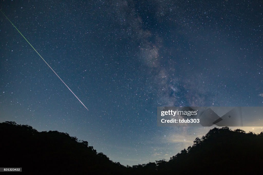 A meteor shoots across the night sky sky leaving a trail of light across the milky way