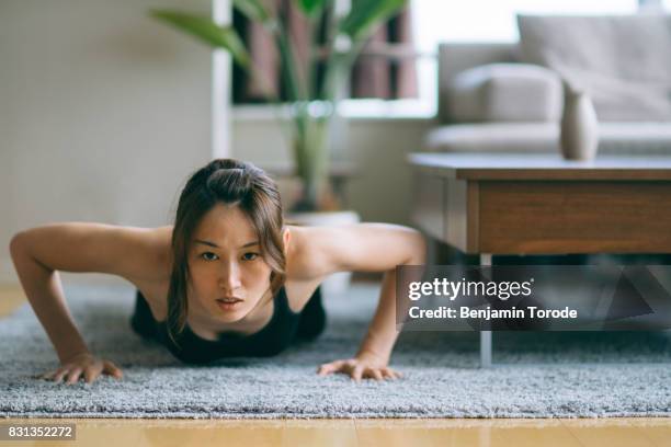 japanese woman in fitness attire performing push-ups on floor of living room - push up japanese imagens e fotografias de stock