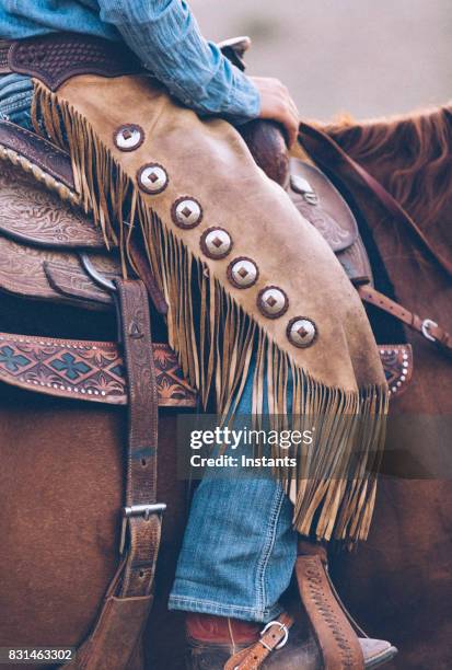 seduta su una sella, dai un'occhiata da vicino all'abbigliamento di una cowgirl con i chaps in pelle, il denim e gli stivali. - imbracatura di pelle foto e immagini stock