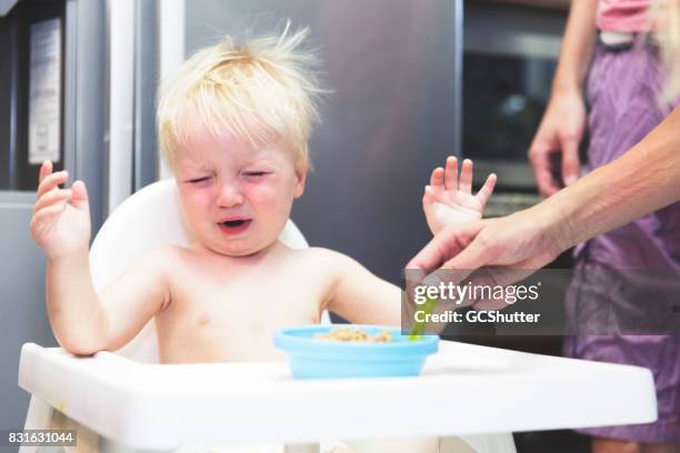 squirming baby trying to push away his breakfast - angry boy stock pictures, royalty-free photos & images