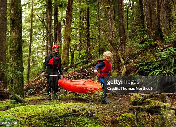 father and son carrying kayak along forest trail - carrying kayak stock pictures, royalty-free photos & images