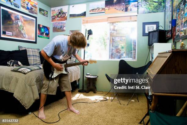 teenage boy playing guitar in bedroom - guitarra eléctrica fotografías e imágenes de stock