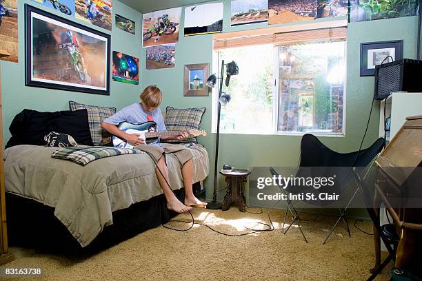 teen boy sitting on bed in bedroom playing guitar - boy sitting on bed stock-fotos und bilder