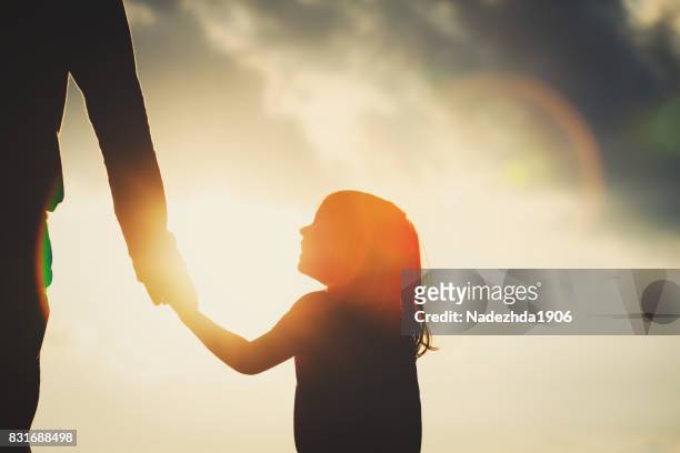 silhouette of little girl holding parent hand at sunset