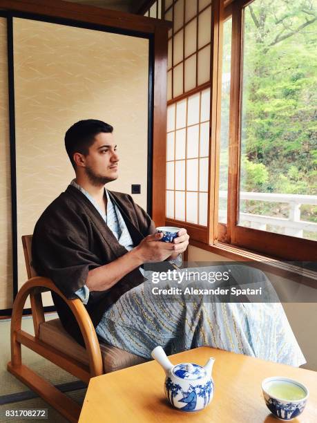 young man wearing yukata drinking green tea in ryokan - ryokan foto e immagini stock