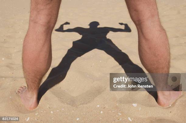 shadow and legs of man flexing muscles on a beach - jambes écartées photos et images de collection