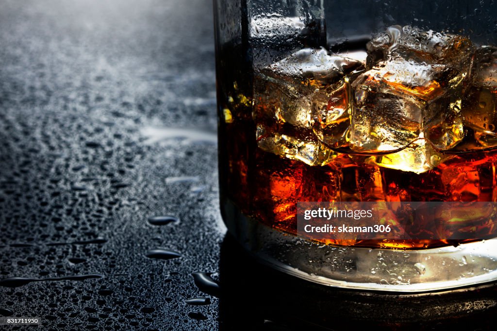 Selective focus pure whisky with ice cube inside whisky glass on wet background