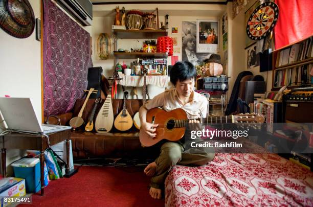 japanese man playing the guitar in his apartment - individuality home stockfoto's en -beelden