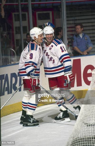 Canadian ice hockey players Adam Graves and Mark Messier of the New York Rangers smile as they celebrate behind the net during a game, 1990s.