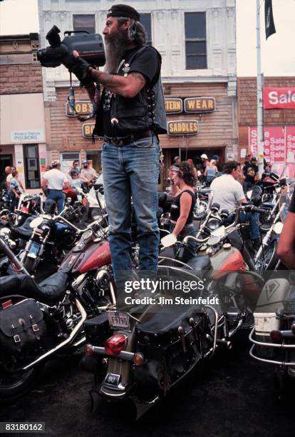 50th Anniversary of the World Famous Sturgis Motorcycle Rally. Bearded man standing on a motorcycle videotaping the rally in Sturgis, South Dakota on...