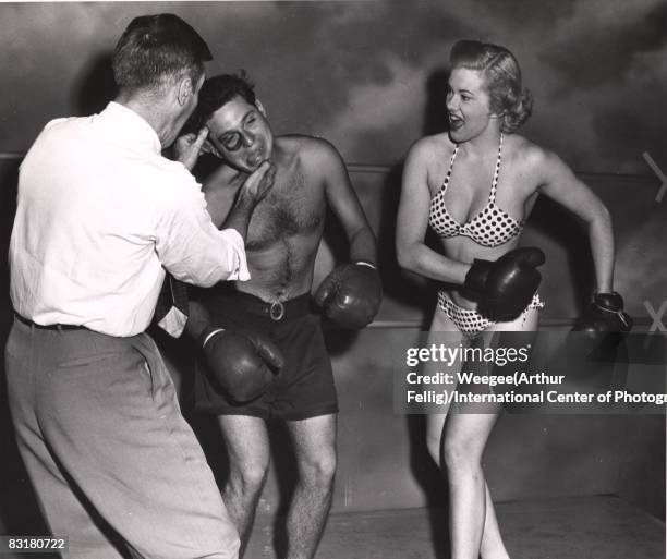 Model in polka dotted bikini and high heels, in boxing ring, knocking out male boxer, with black eye, New York, ca.1950s.