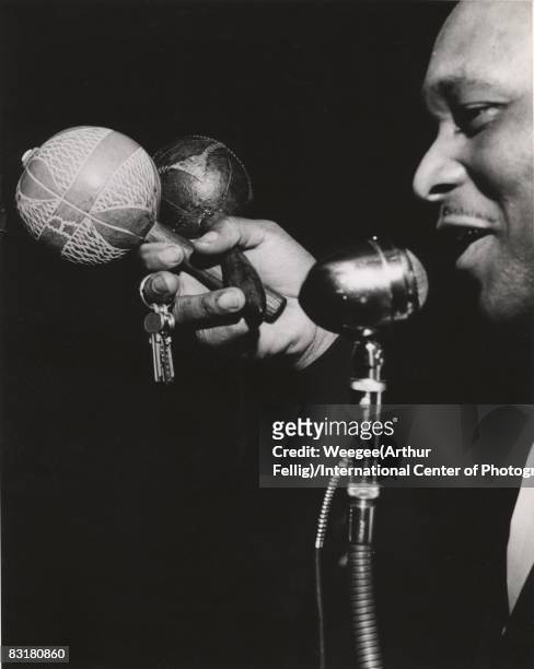 Man holding musical instruments, maracas and keys, sings into a microphone while performing at an unidentified venue, New York, ca.1944.
