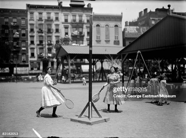 Two girls play swingball or totem tennis, a variation of tetherball, on an outdoor playground, New York, ca.1920s.