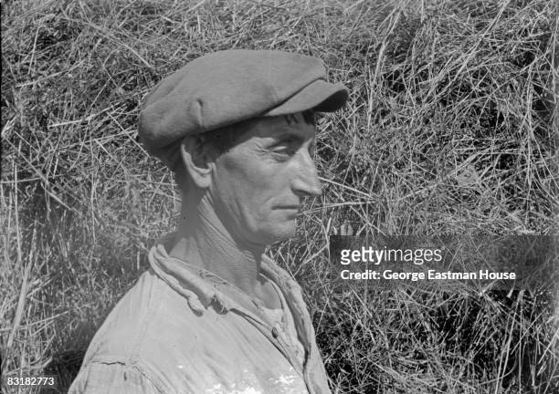 Portrait of a farmer from an unidentified region of upstate New York. He poses in profile while wearing a hat, with a haystack standing as...