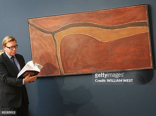 Sotheby's head of Aboriginal Art, Tim Klingender, flicks through a catalogue as he stands next to a painting by famous Aboriginal artist Rover Thomas...