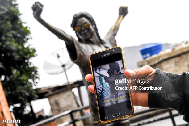 Tourist guide shows a mobile phone with the picture of US pop icon Michael Jackson´s statue with an assault rifle hanging around its neck at Santa...