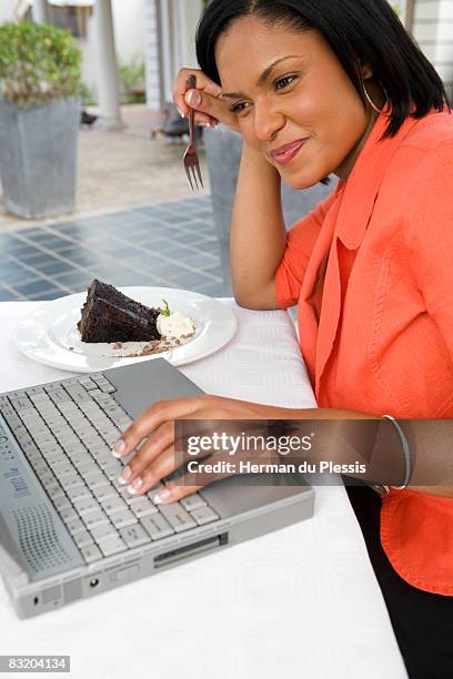 woman working on laptop computer while eating chocolate cake, franschhoek, western cape province, south africa - convenience chocolate stock pictures, royalty-free photos & images