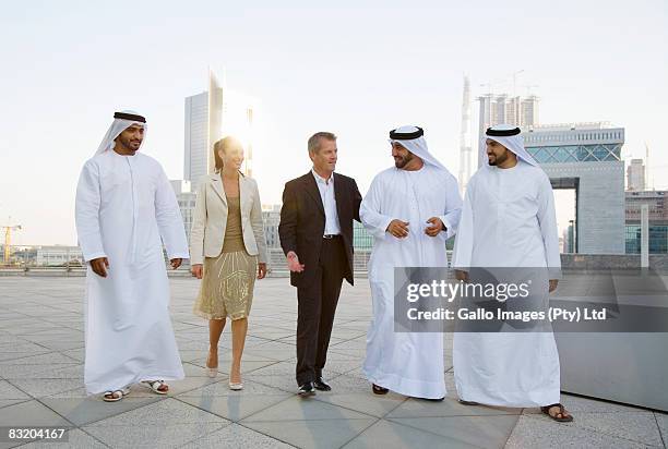 man and woman meeting with men in traditional middle eastern attire, dubai cityscape in background, uae - dubai difc stock pictures, royalty-free photos & images