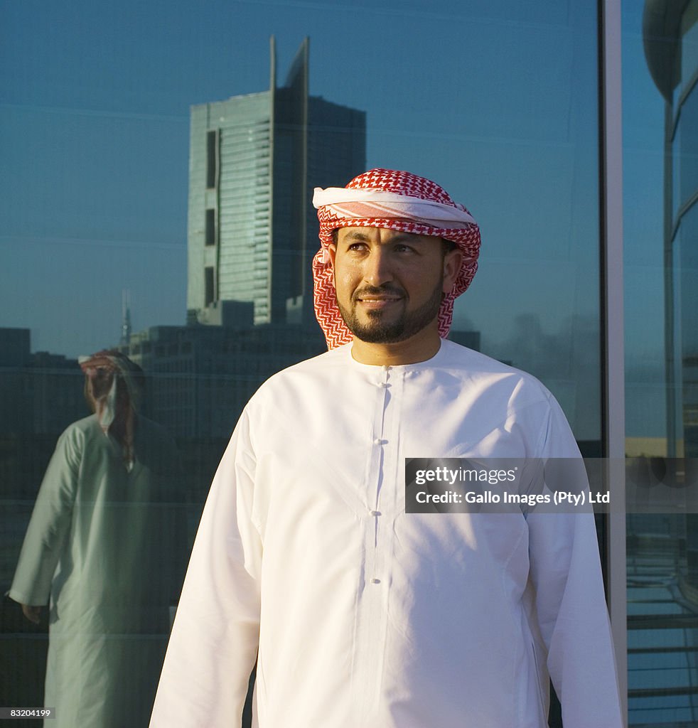Man dressed in traditional Middle Eastern attire reflected in glass window, Dubai, UAE