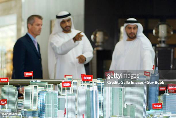 view of property model in foreground and men in traditional middle eastern dress meeting western businessman, dubai, uae - dubai difc stock pictures, royalty-free photos & images