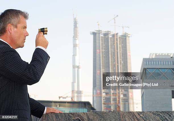 businessman looking through galilean binoculars at dubai cityscape, uae - difc stockfoto's en -beelden