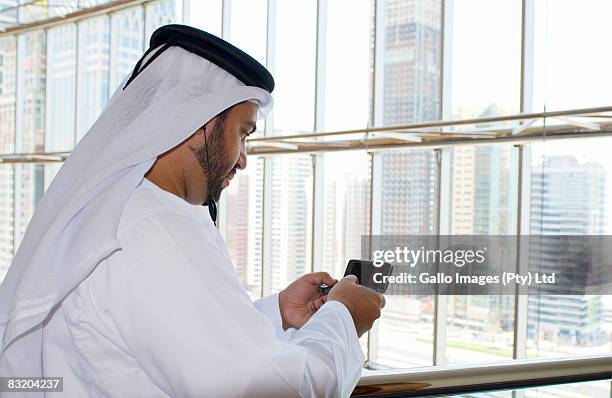 side view of man in middle eastern traditional dress using phone, dubai cityscape in background, uae - difc stock-fotos und bilder