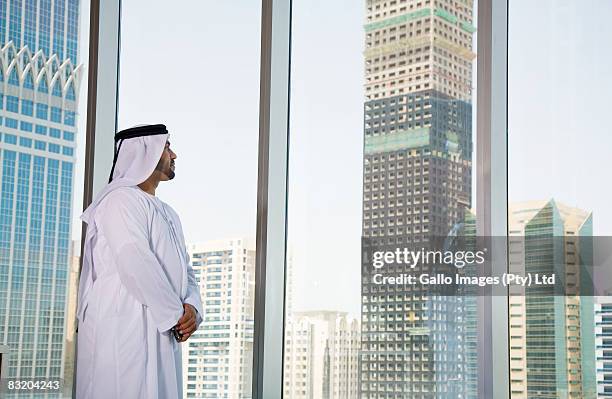 man in middle eastern traditional dress looking out at dubai cityscape, uae - difc stockfoto's en -beelden