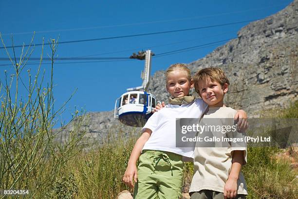 low angle view of boy and girl on the side of table mountain with cable car in background, cape town, western cape province, south africa - cape town cable car stock pictures, royalty-free photos & images