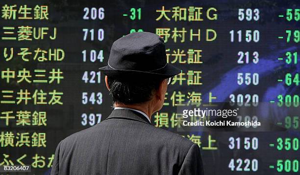 Man looks at an electronic board displaying falls in share prices on October 10, 2008 in Tokyo, Japan. The Nikkei 225-issue stock index falls below...