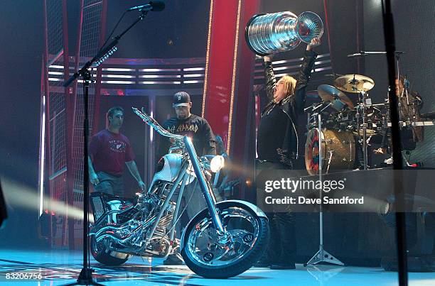 Joe Elliott of Def Leppard hoists the Stanley Cup while Darren McCarty and Kyle Quincy both of the Detroit Red Wings stand by during NHL Face-Off...