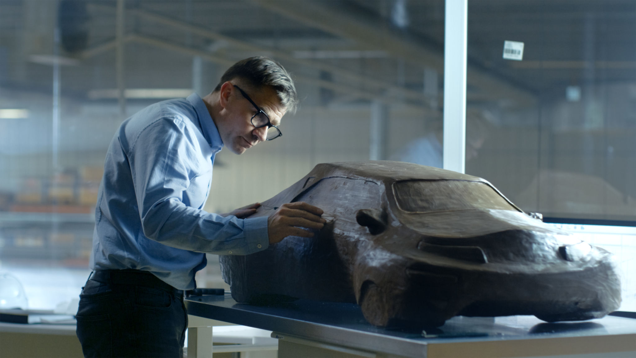 Chief Automotive Designer with Rake Sculpts Futuristic Car Model from Plasticine Clay. He Works in a Special Studio Located In a Large Car Factory. Chief Automotive Designer with Rake Sculpts Futuristic Car Model from Plasticine Clay. He Works in a Special Studio Located In a Large Car Factory.