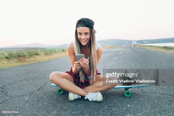 schöne frau sitzen auf skateboard auf landstraße - longboard skating stock-fotos und bilder