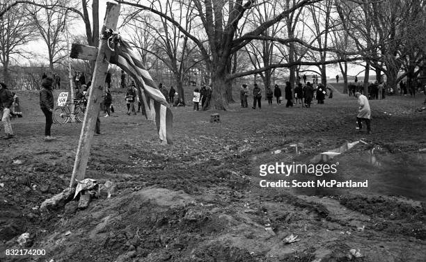 Washington, DC : Wooden stakes in the shape of a cross are driven into the mud, and adorned with an American Flag, as activists walk through the mud...