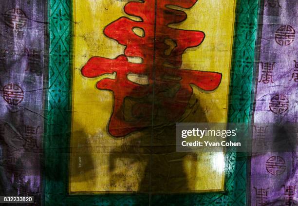 The shadowy form of a Chinese Opera performer is perceived through the stage backdrop during a performance in the Chinatown area of Bangkok.