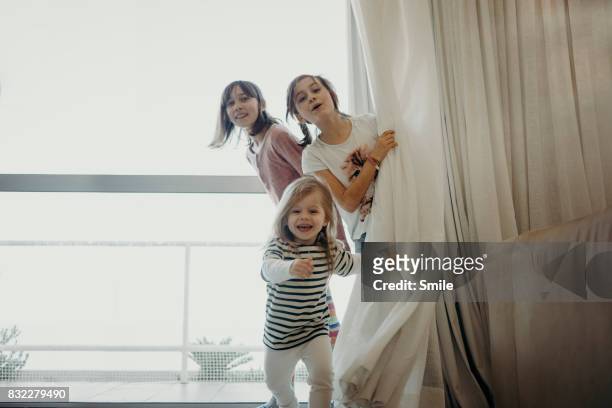 three young girls peer from behind curtain - running indoors stock pictures, royalty-free photos & images