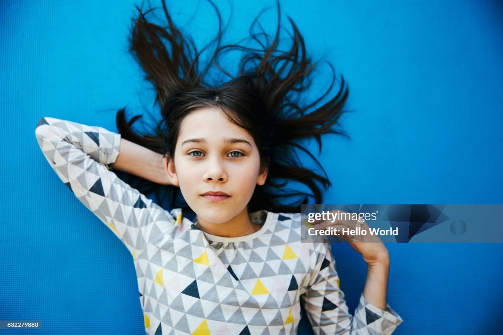 Girl lying on blue background, looking at camera