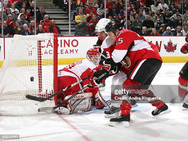 Chris Neil of the Ottawa Senators digs for a rebound against Chris Osgood and Andreas Lilja of the Detroit Red Wings at Scotiabank Place on October...