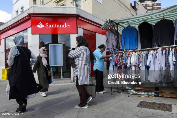 People pass a bank branch of Banco Santander SA near a market in London, U.K., on Tuesday, Aug. 15, 2017. Banco Santander, Spains biggest lender, has...