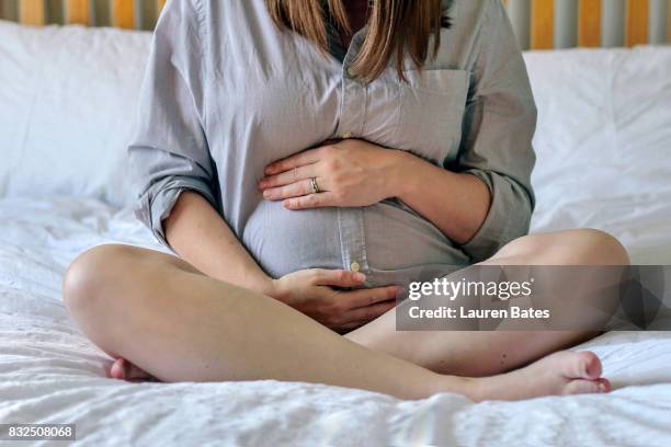 pregnant woman sitting on bed - woman holding tummy stock-fotos und bilder