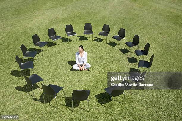 businesswoman sitting in circle of office chairs in field - omgeven stockfoto's en -beelden
